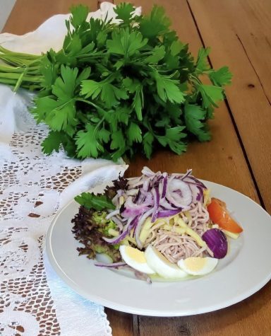 Ein Teller mit Salat, Zwiebeln, Eiern und frischer Petersilie auf einem Tisch.