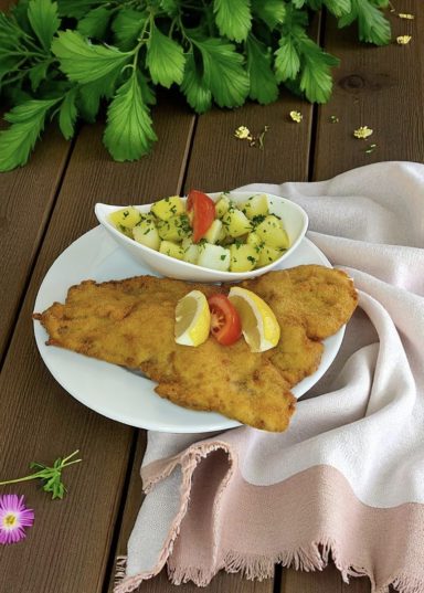 Frittierter Fischfilet mit Zitrone und Beilagensalat auf einem Teller.